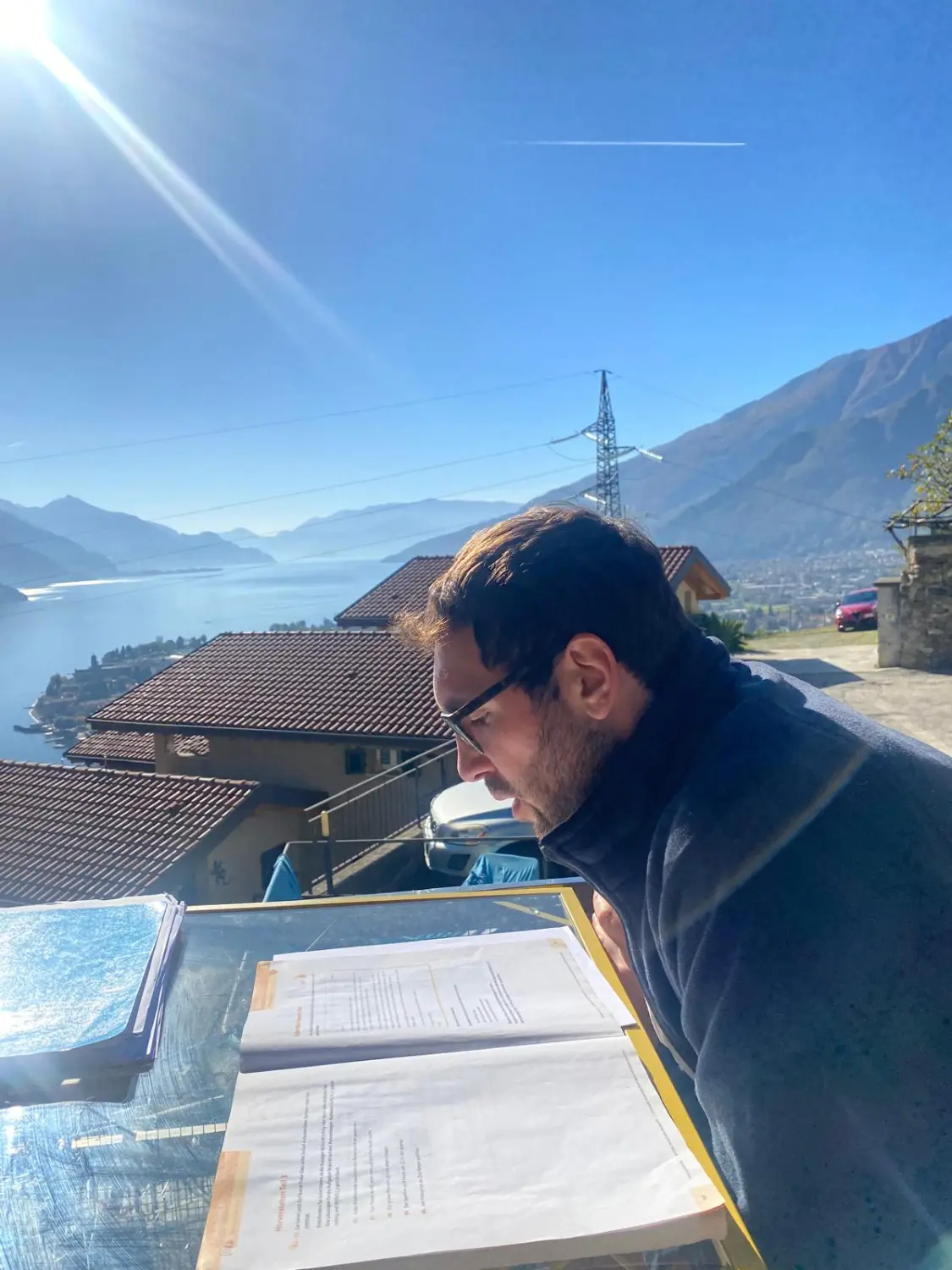 SprachHaus Bamberg - uomo che studia un libro con vista sulle montagne e sul lago sullo sfondo